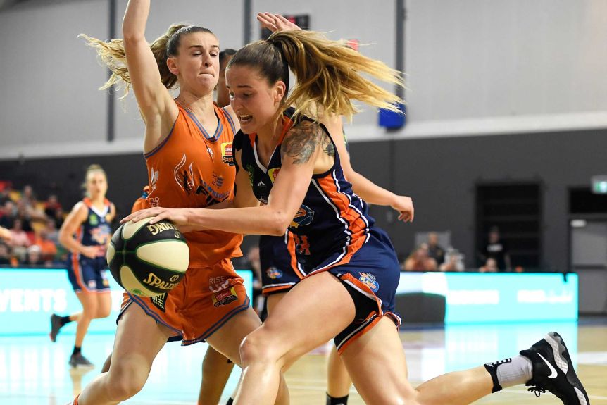 A WNBL player bounces a basketball while being defended against by an opponent.